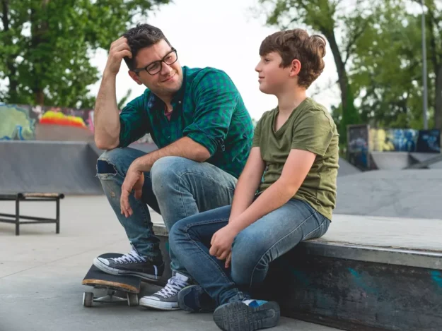 Support Worker Sat With Young Person At Skate Park